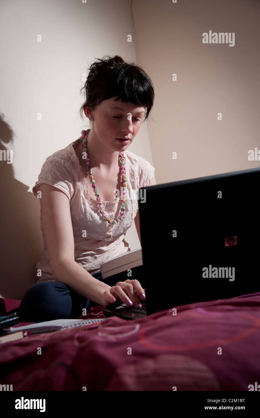 Una giovane donna UK università studenti che lavorano sul suo computer portatile nella sua camera da letto a casa Foto Stock