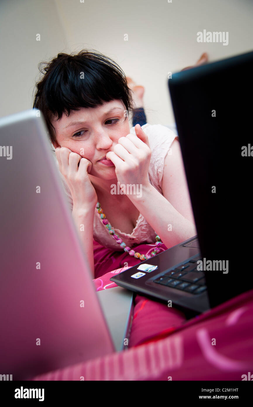 Una giovane donna UK università studenti che lavorano sui suoi 2 due computer laptop nella sua camera da letto a casa Foto Stock
