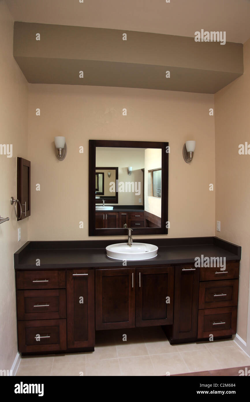 Singolo lavello vanità con cabinet in legno e specchio che riflette il resto della stanza da bagno residenziale Foto Stock