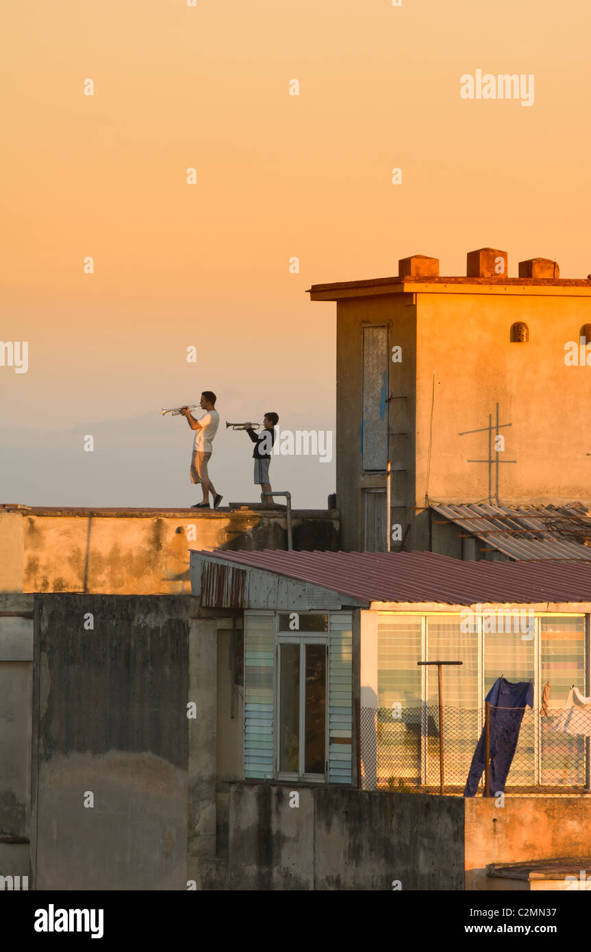 Uomo e ragazzo suonare la tromba su un tetto al tramonto, Camaguey, Cuba Foto Stock