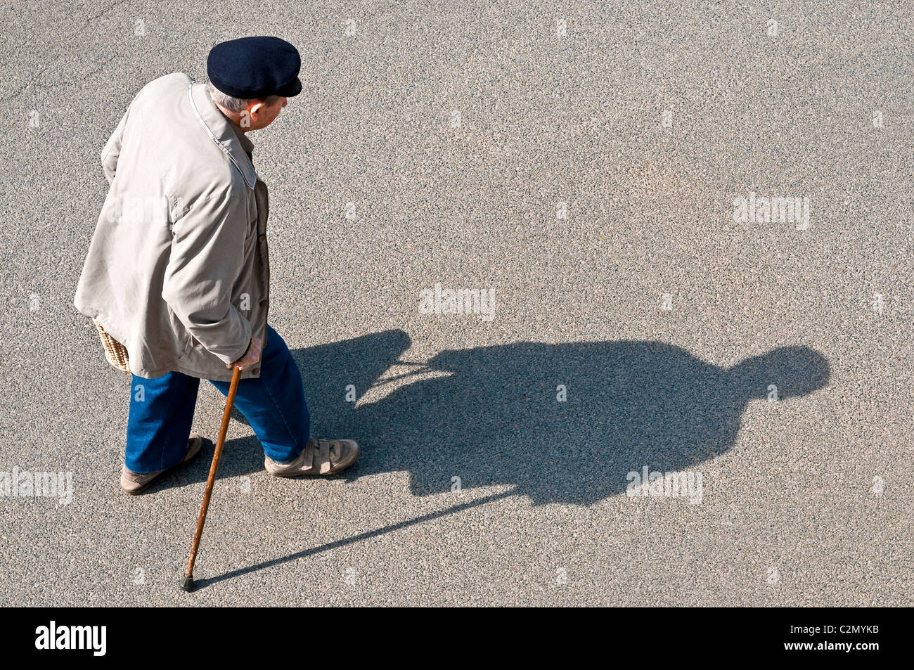 Il vecchio uomo camminando per strada con colata di bastone lungo ombra - Francia. Foto Stock