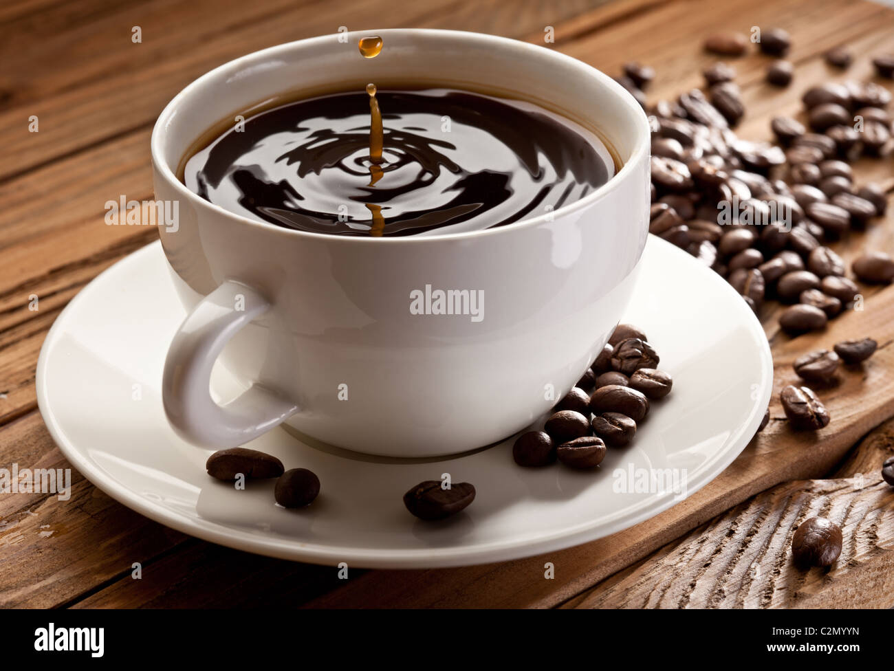 Goccia che cade in una tazza di caffè. Su uno sfondo di legno Foto Stock