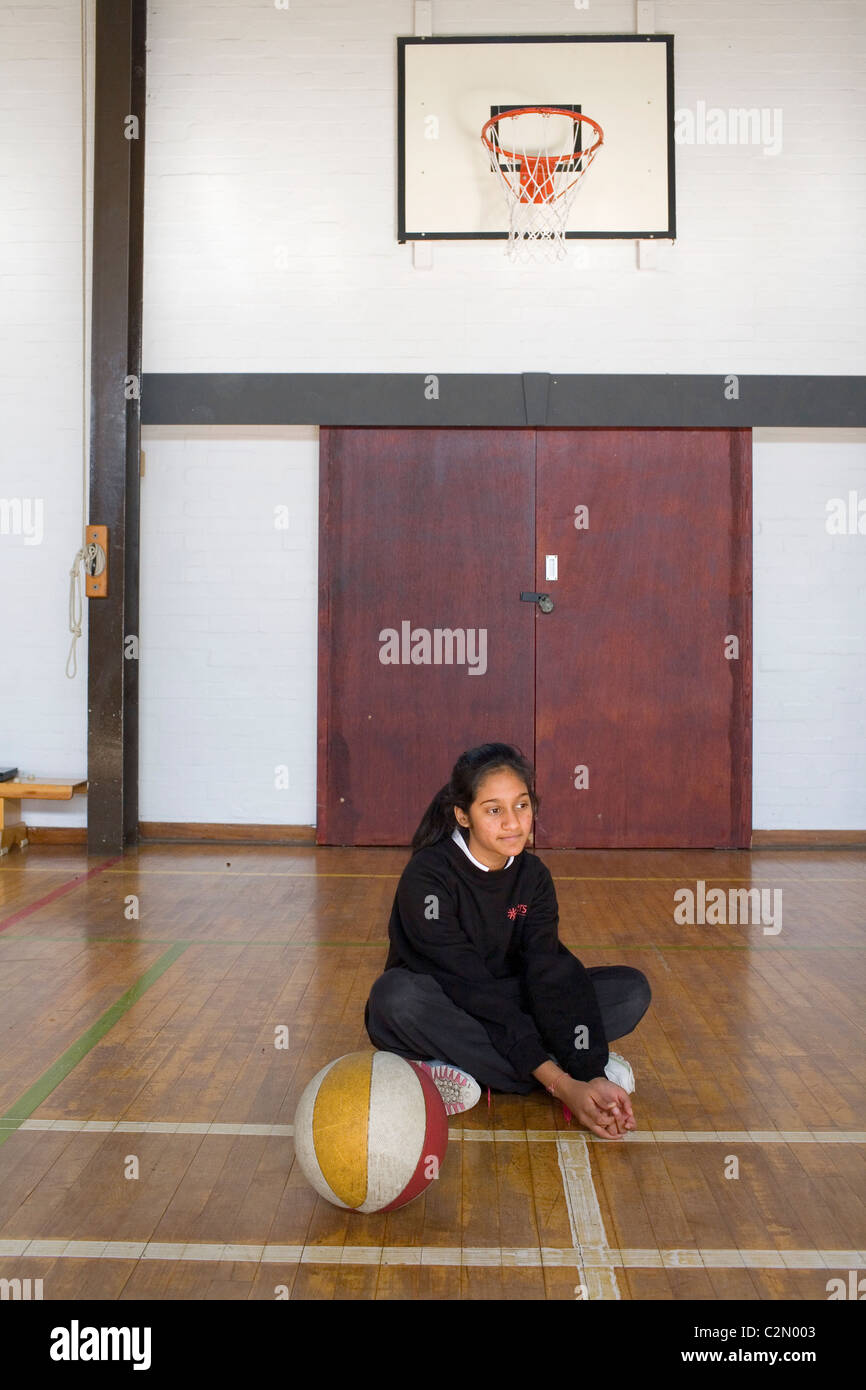 Un ragazzo asiatico sat nella palestra della scuola con una palla da basket. Foto Stock