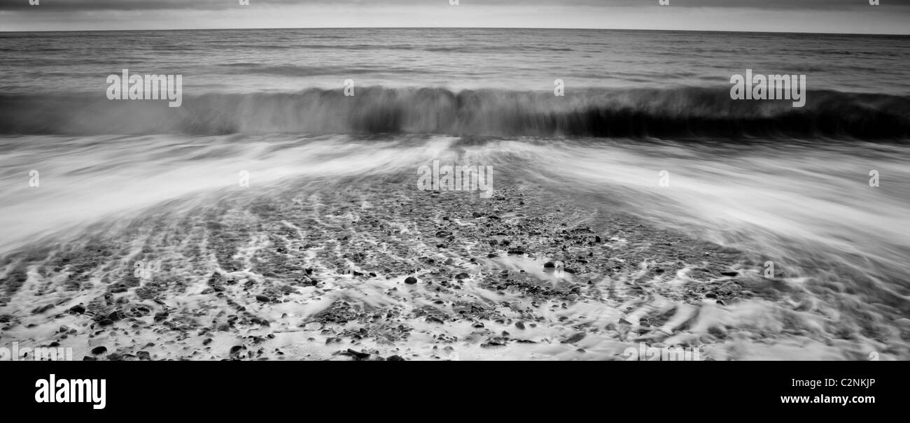 Onde che si infrangono sulla spiaggia di ciottoli in bianco e nero Foto Stock