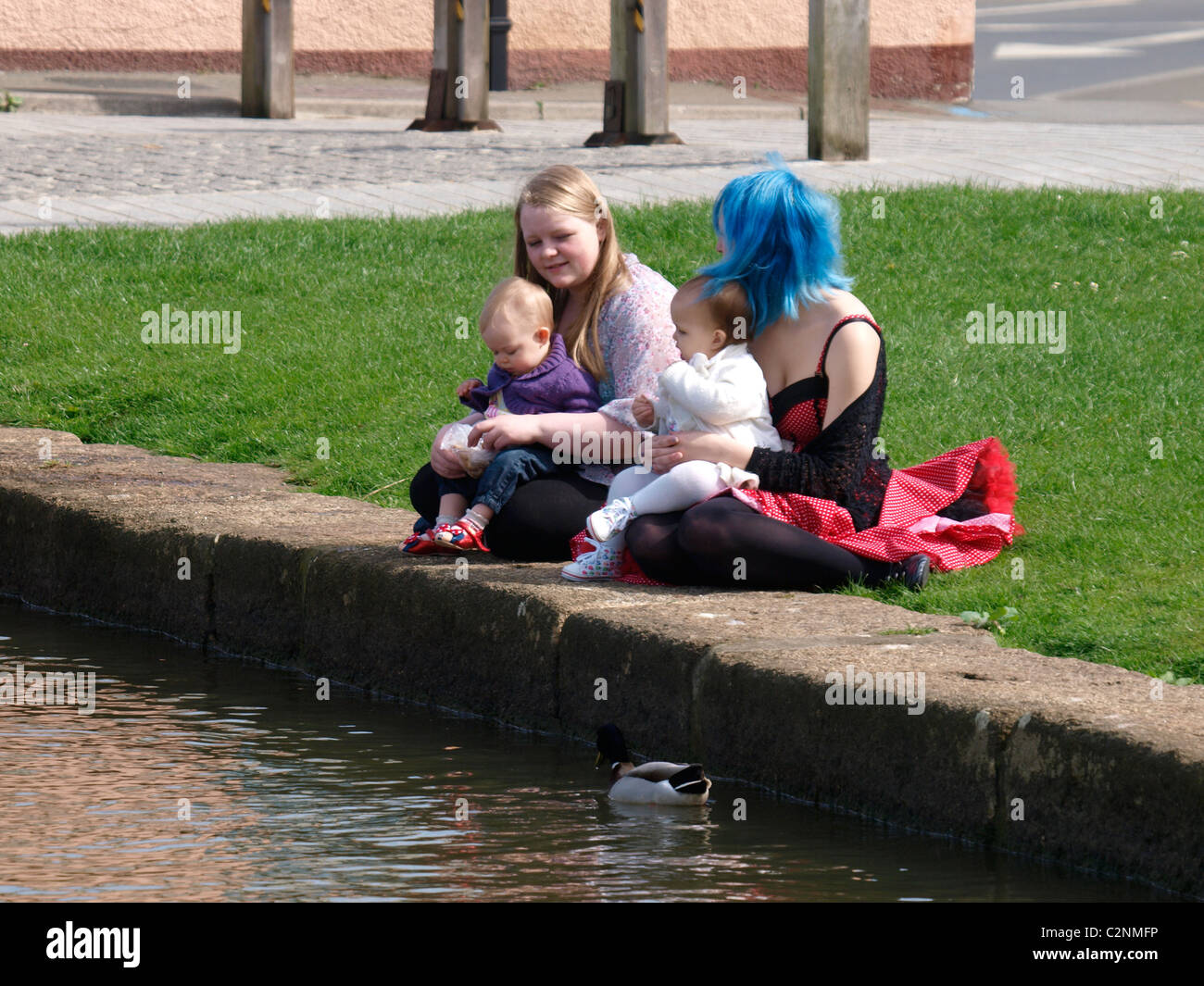 Due giovani mamme e bambini sat dall'acqua di alimentazione di anatre, Bude, Cornwall, Regno Unito Foto Stock