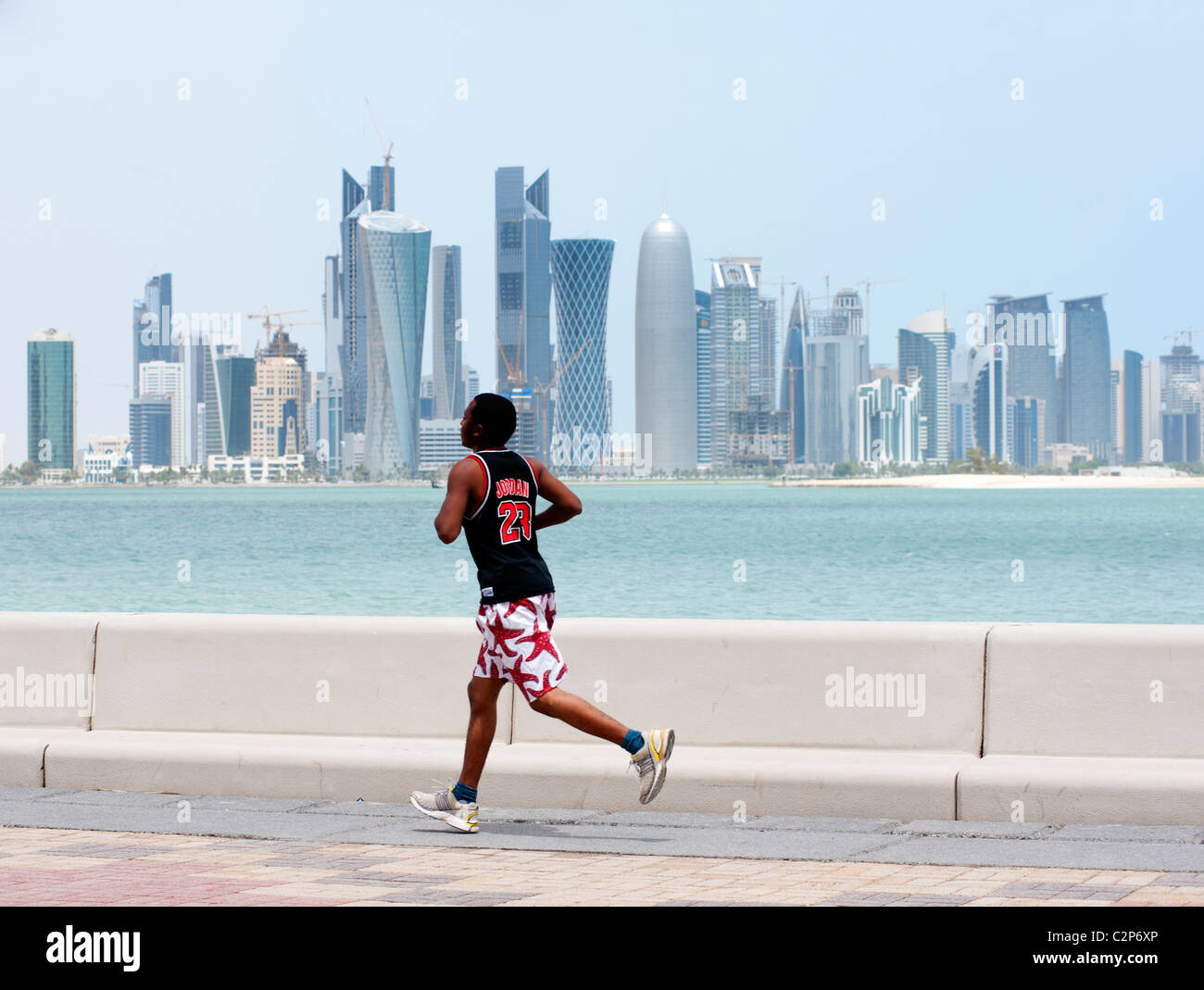 Uomo che corre lungo la corniche waterfront con skyline della città in distanza a Doha in Qatar Foto Stock