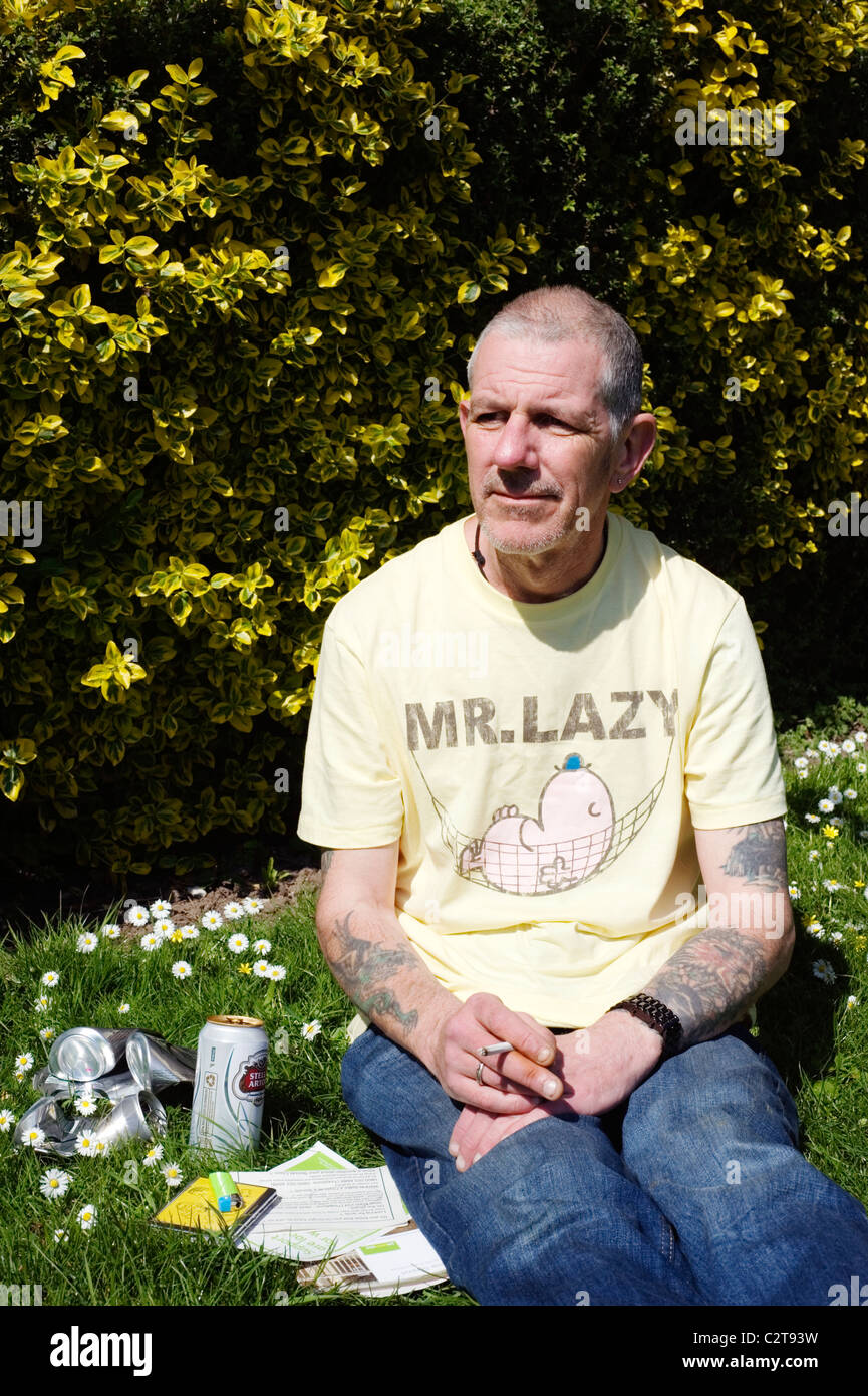 Disoccupati uomo nel parco pubblico godendo il sole con benefici volantini birra e sigarette Foto Stock