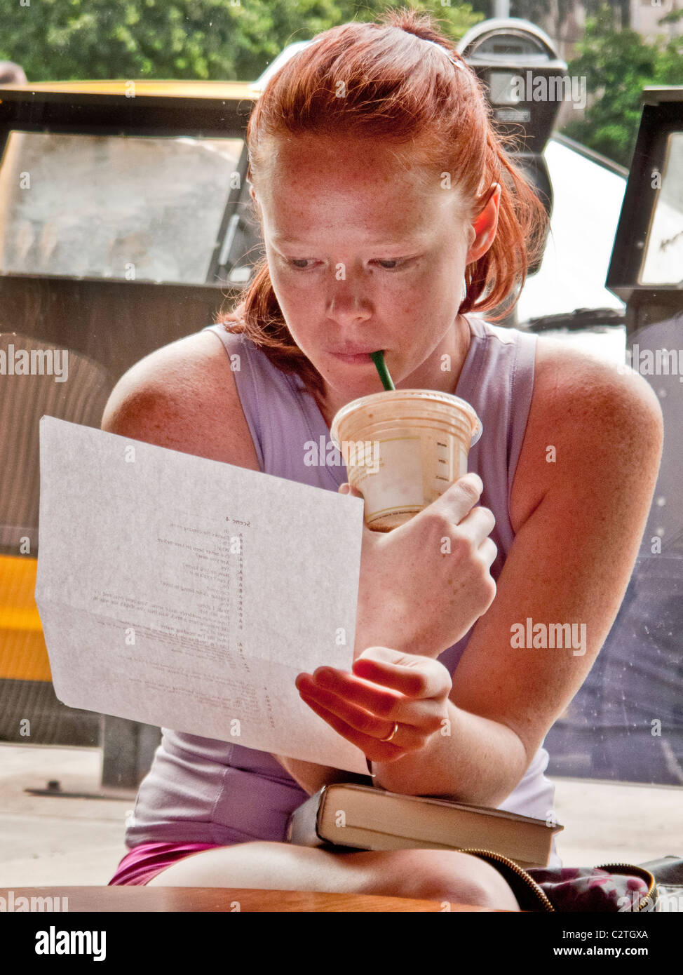 Mentre si beve caffè ghiacciato, una giovane donna legge un collegio assegnazione intensamente a una libreria di Santa Monica, CA. Foto Stock
