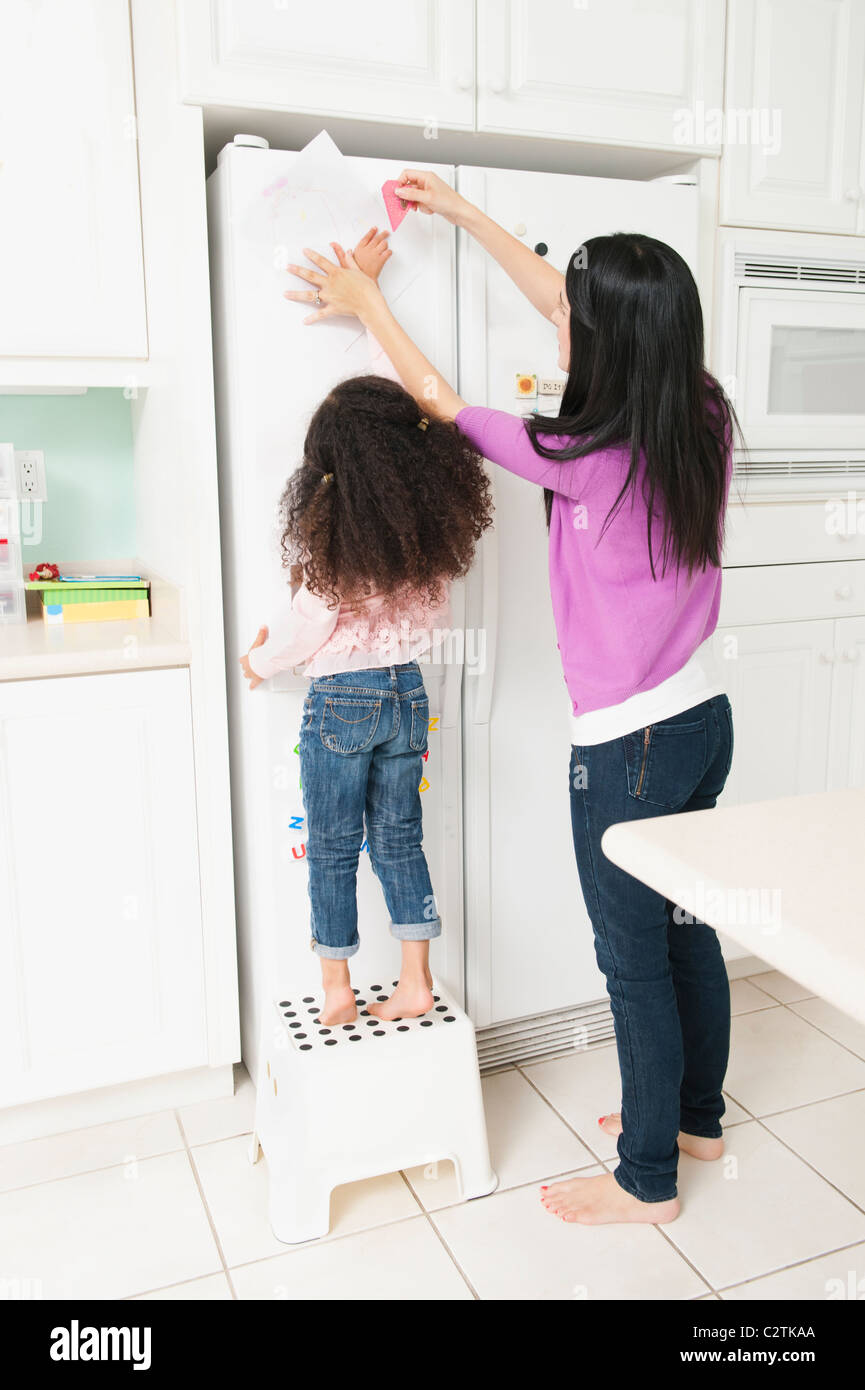 Madre figlia mettendo il disegno sul frigorifero Foto Stock