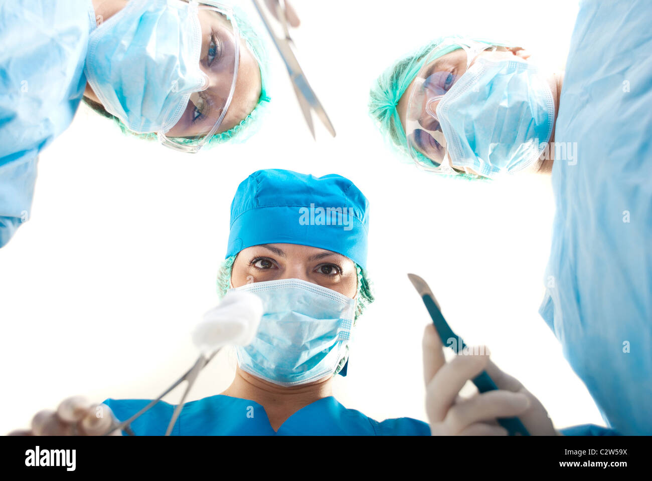 Vista dal basso del tre chirurghi in funzionamento tenendo gli strumenti chirurgici Foto Stock