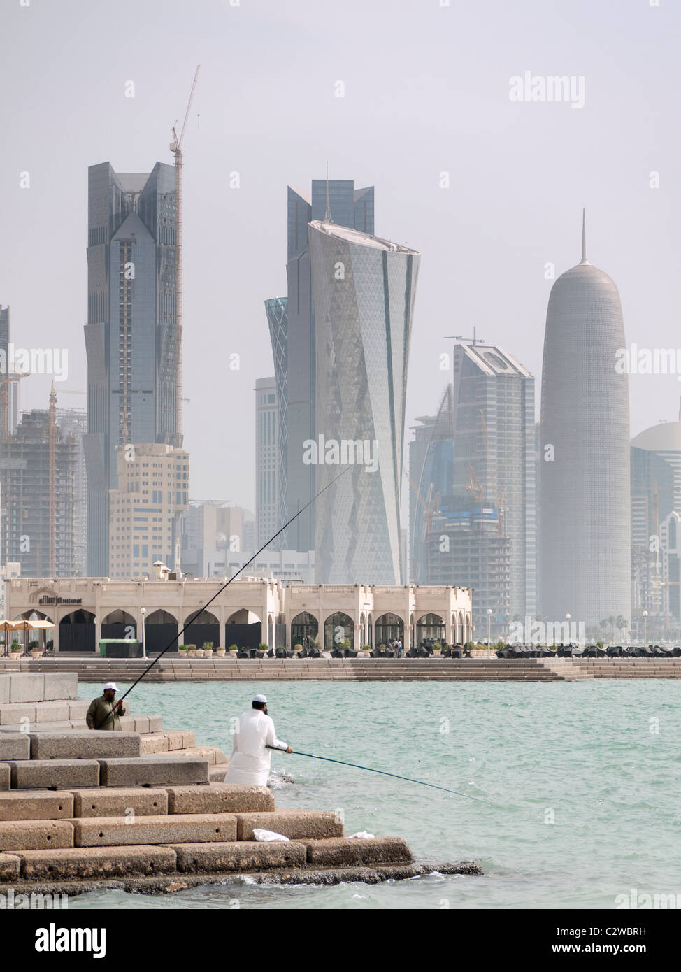 Gli uomini la pesca sulla Corniche con moderne torri di uffici e sullo skyline nel quartiere degli affari a Doha in Qatar Foto Stock