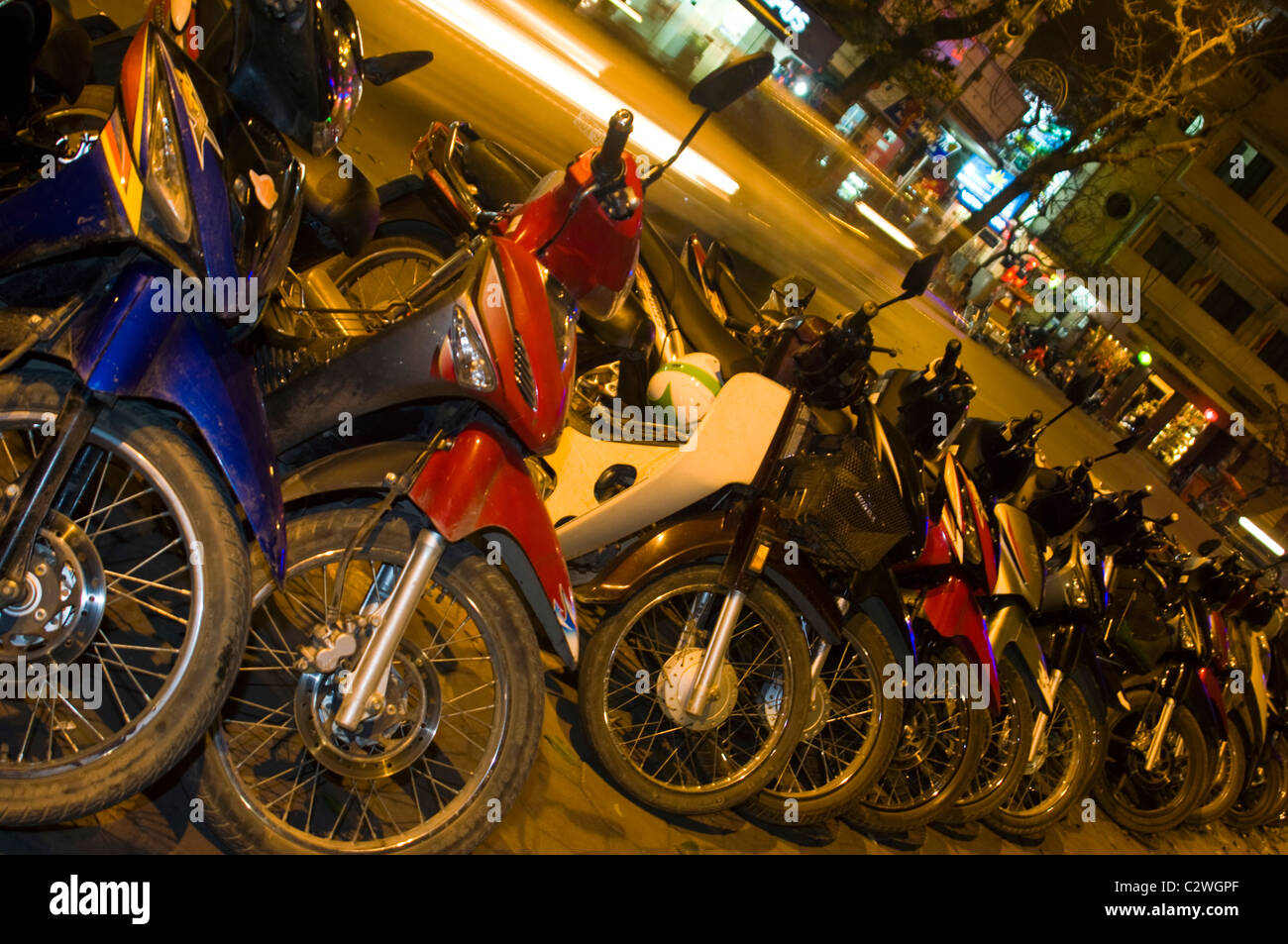 Vista orizzontale di una linea di ciclomotori e scooter parcheggiato sul marciapiede in una fila di Hanoi di notte. Foto Stock