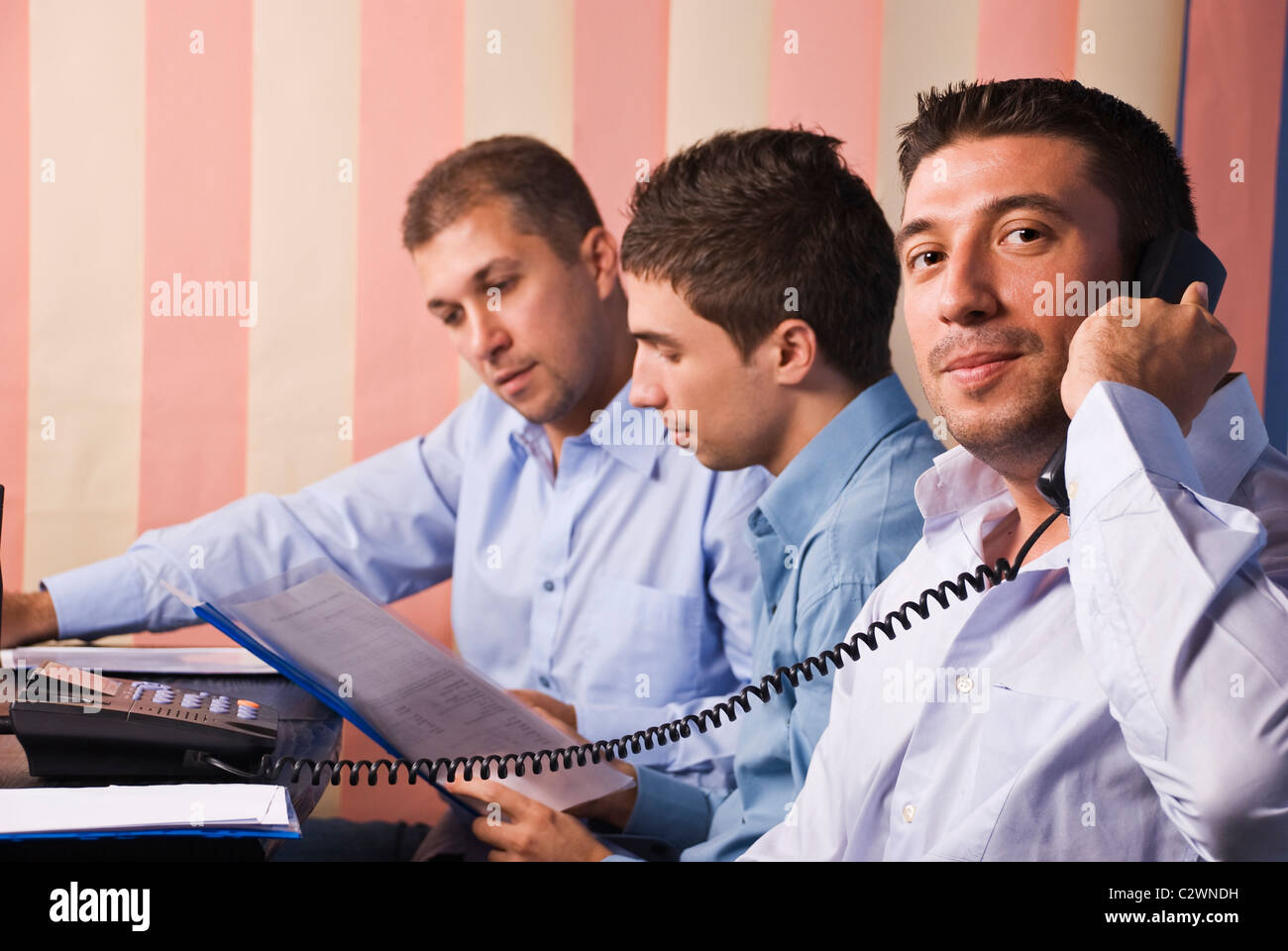 Tre uomini di affari in office,concentrarsi sul primo uomo che parla al telefono e gli altri due uomini e di lettura avente una conversazione Foto Stock