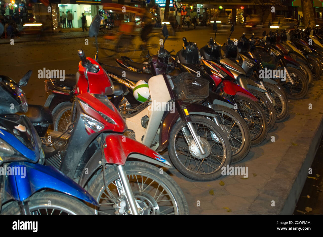 Vista orizzontale di una linea di ciclomotori e scooter parcheggiato sul marciapiede in una fila di Hanoi di notte. Foto Stock