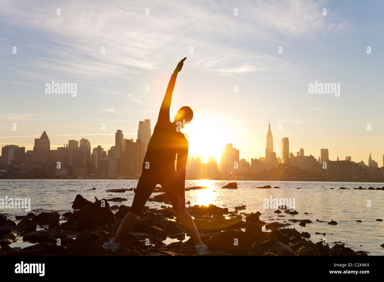 Una donna runner allungamento in una posizione di yoga nella parte anteriore dello skyline di Manhattan, New York City, Stati Uniti d'America, all'alba sunrise. Foto Stock