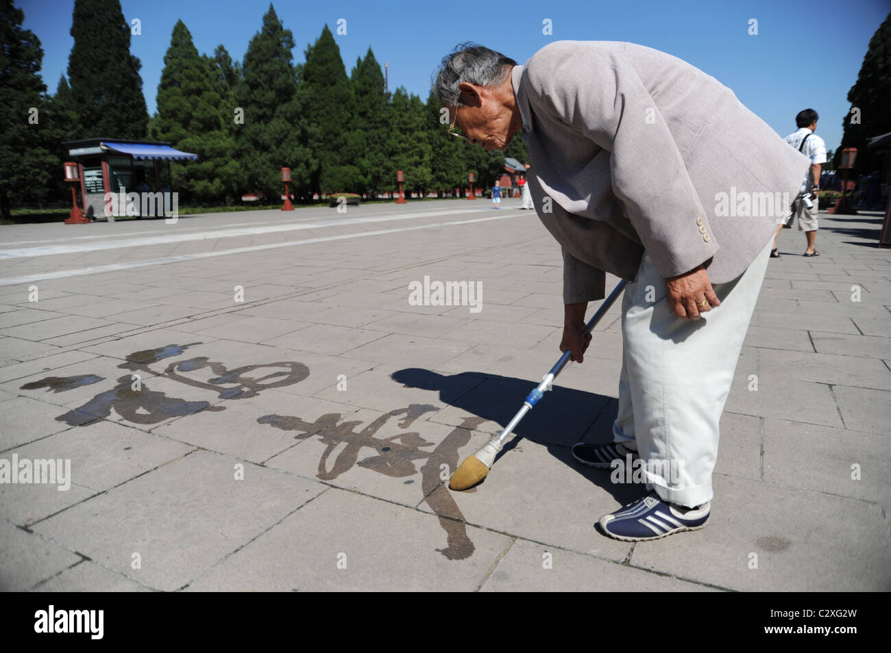 Un vecchio uomo Cinese scrittura calligrafia su terra con un pennello grande e acqua Foto Stock