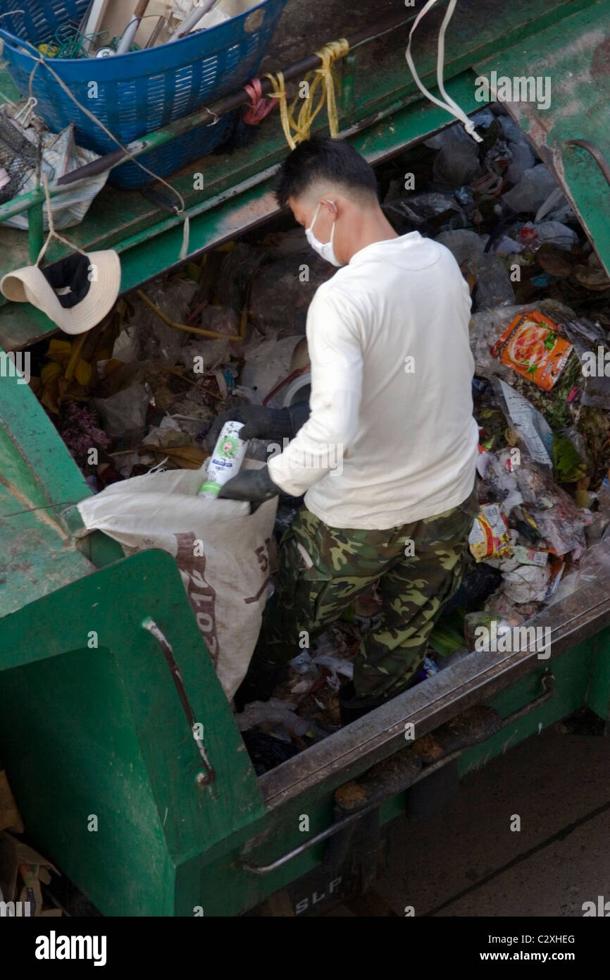 Un uomo è in piedi nel cestino durante il caricamento di un camion della spazzatura su una strada di città in Mae Sai, (SAE) Thailandia. Foto Stock