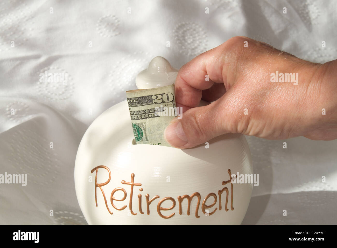 Un uomo collocando un american 20 dollar nota in un 'retirement risparmi dei contenitore. l'immagine è illuminata dalla luce della finestra Foto Stock