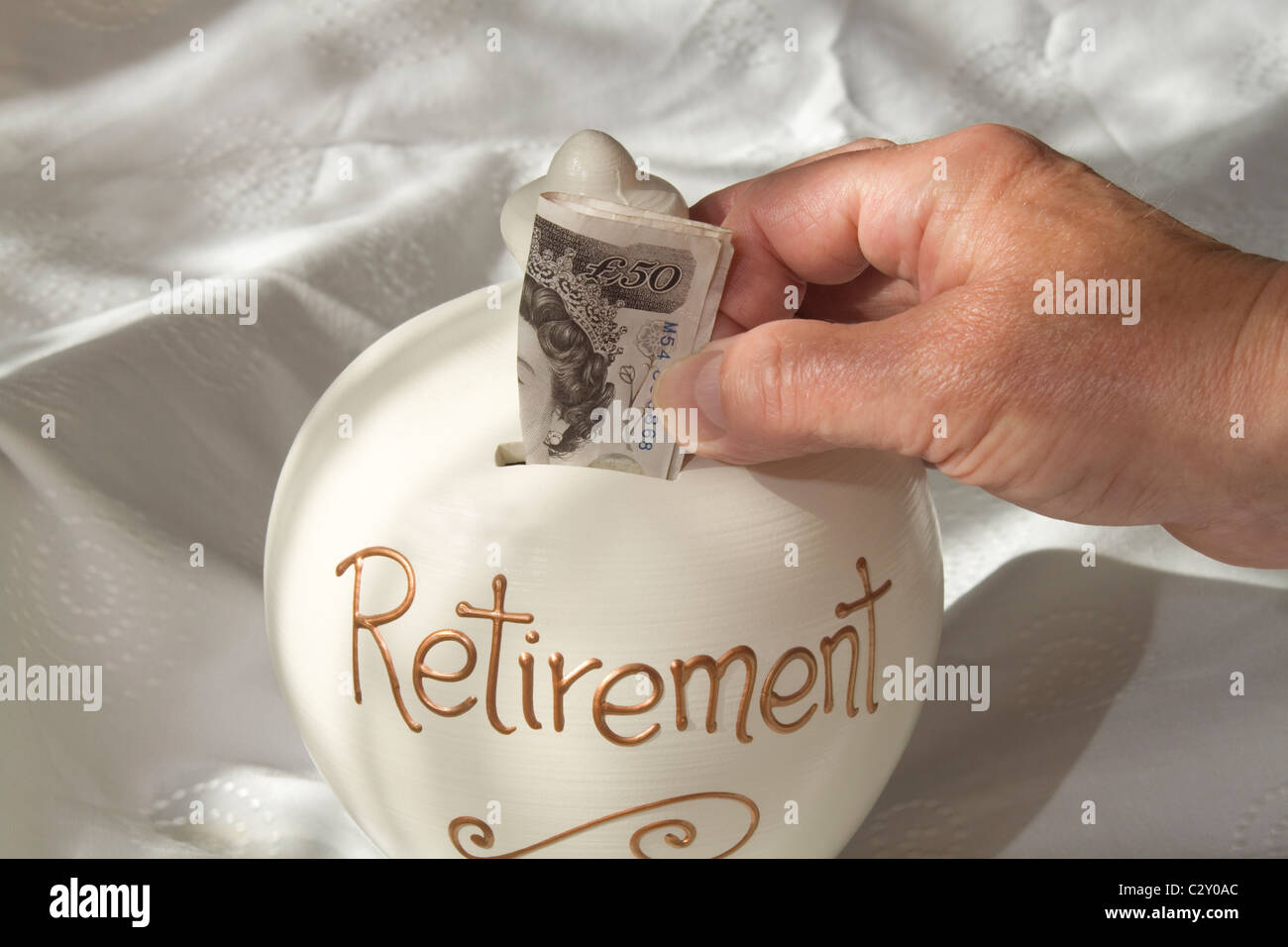 Un uomo collocando un british £50 nota in un 'retirement risparmi dei contenitore. l'immagine è illuminata dalla luce della finestra Foto Stock
