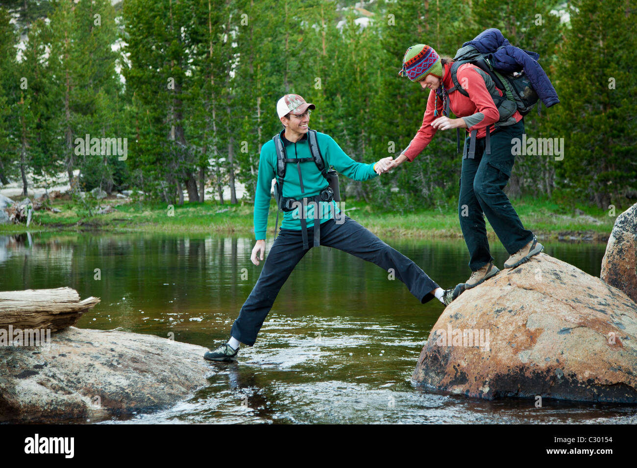 Un giovane uomo afferra la mano della sua fidanzata come egli aiuta la sua attraverso un ruscello di montagna. Foto Stock
