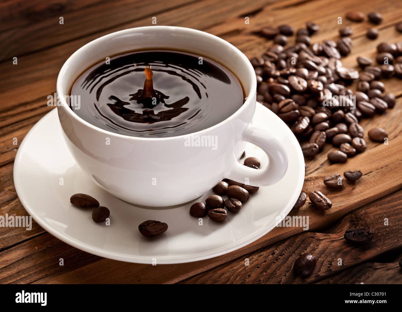 Goccia che cade in una tazza di caffè. Su uno sfondo di legno Foto Stock