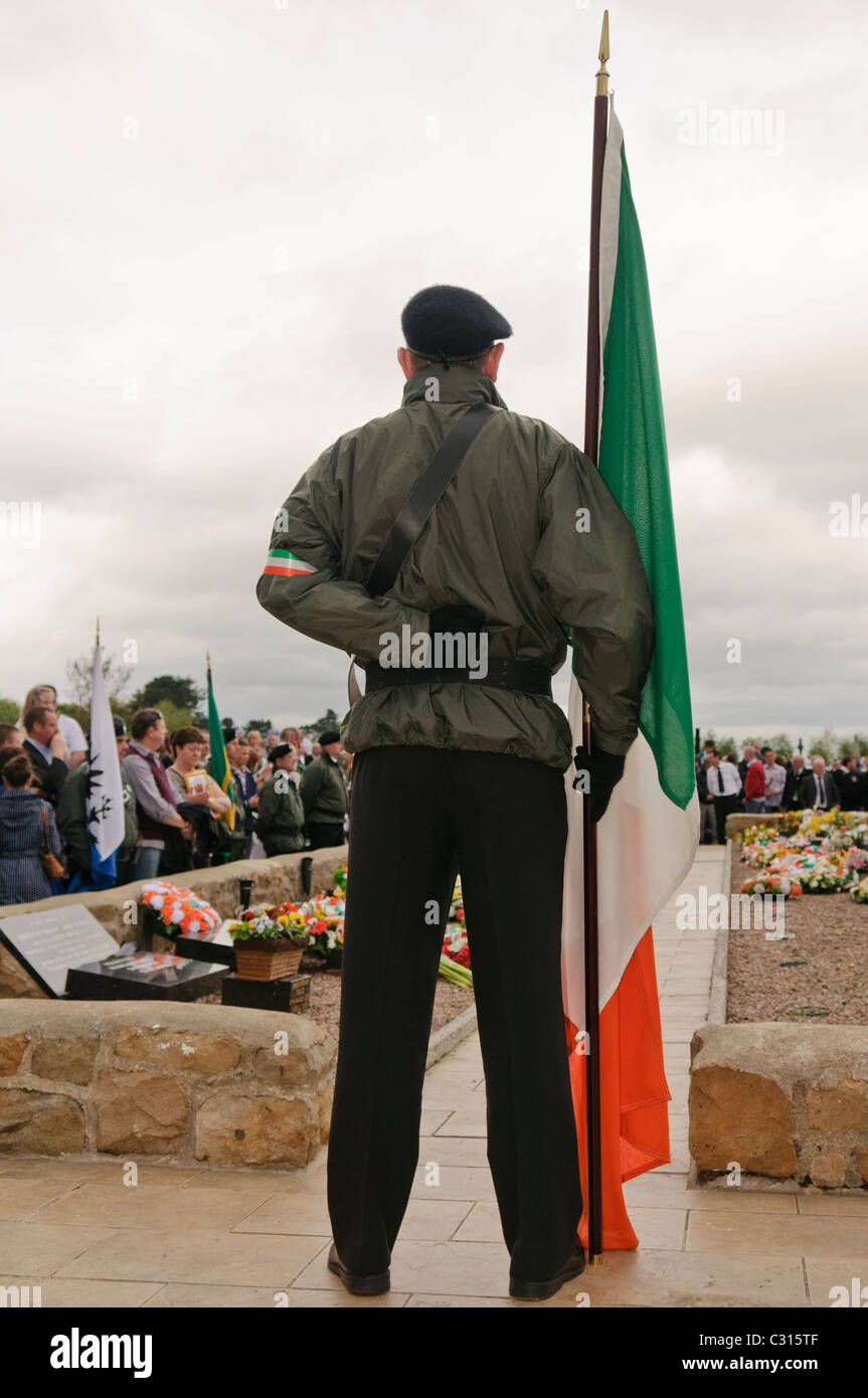 Uomo in uniforme paramilitare detiene un Irish bandiera tricolore presso l'IRA complotto repubblicano Foto Stock
