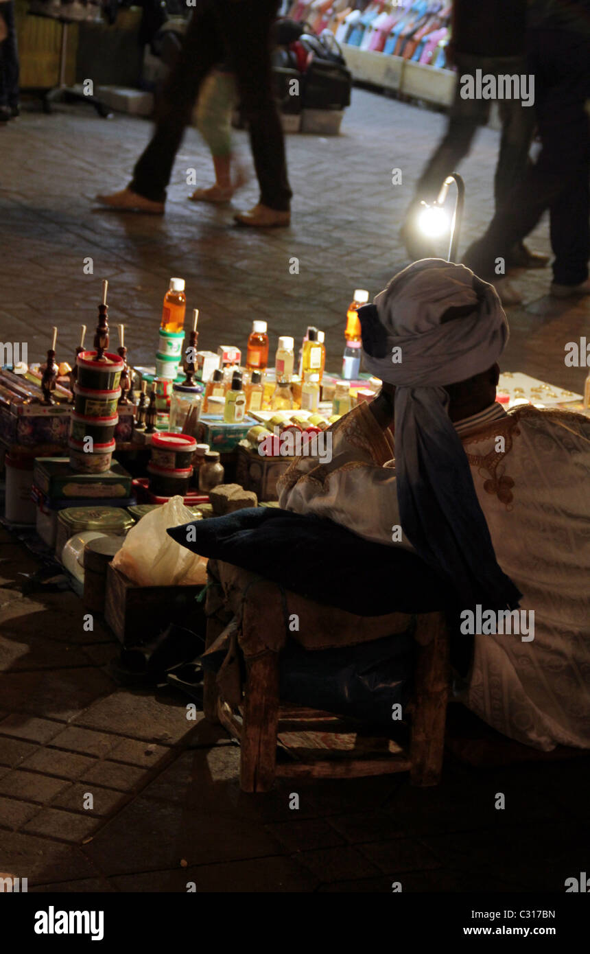 Uomo appoggiato a una fase di stallo in Piazza Jamaa El Fnaa, mercato di Marrakesh la vendita di profumi e ninnoli di notte Foto Stock