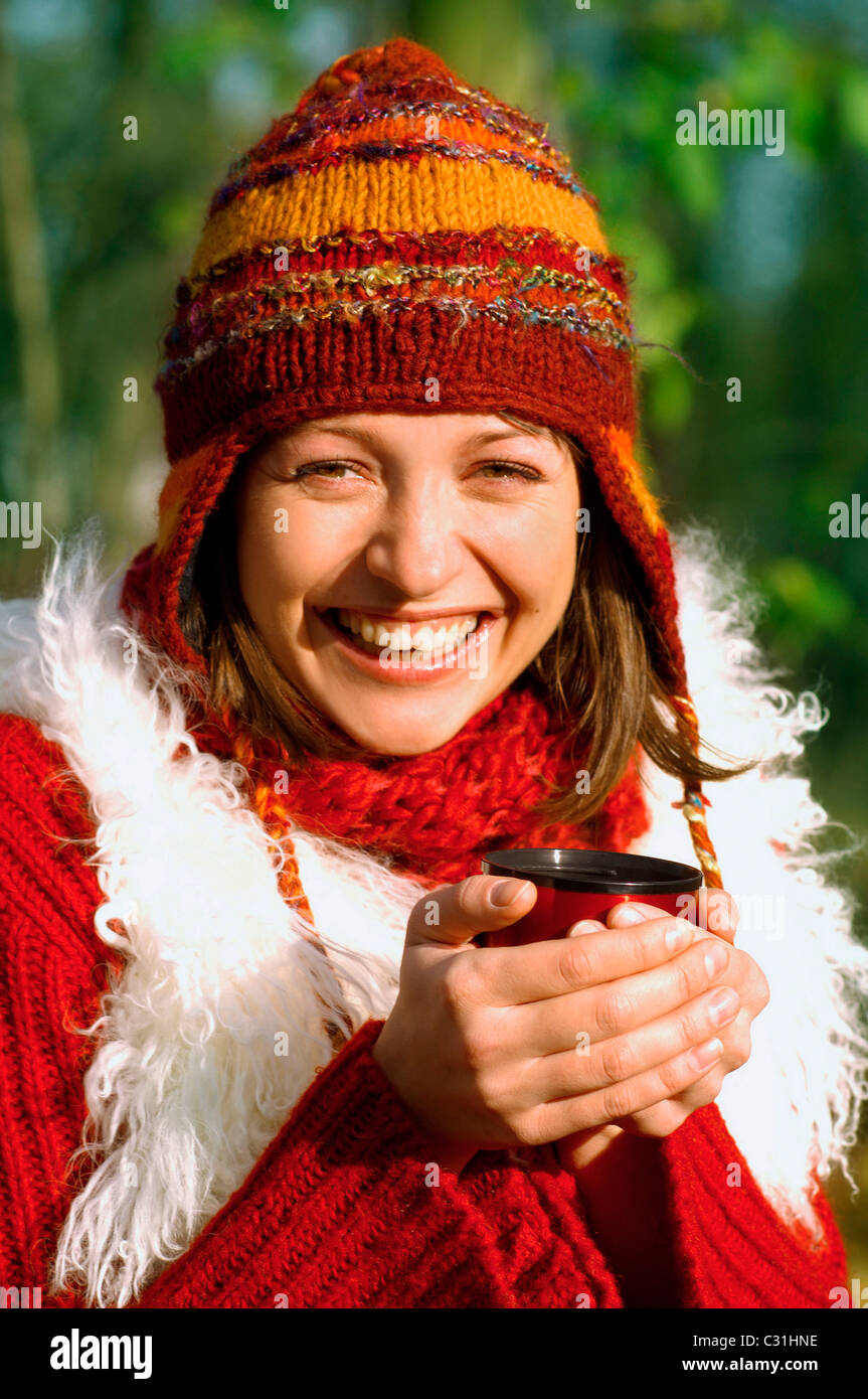 Giovane donna il riscaldamento se stessa con una bevanda calda mentre in una passeggiata nella foresta Foto Stock