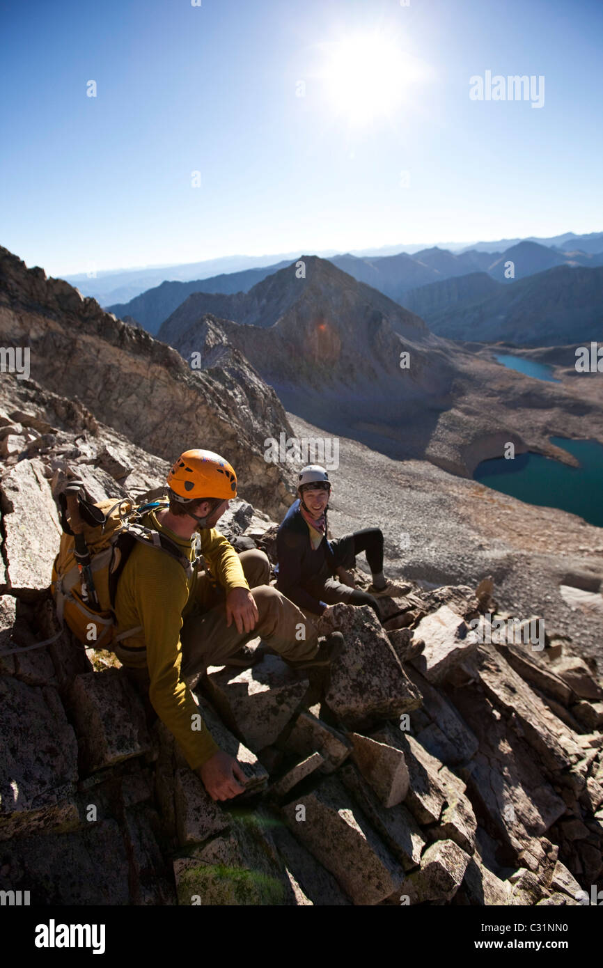 Due giovani uomini di sedersi su un esposto linea di cresta prendendo una pausa mentre arrampicata in montagna. Foto Stock