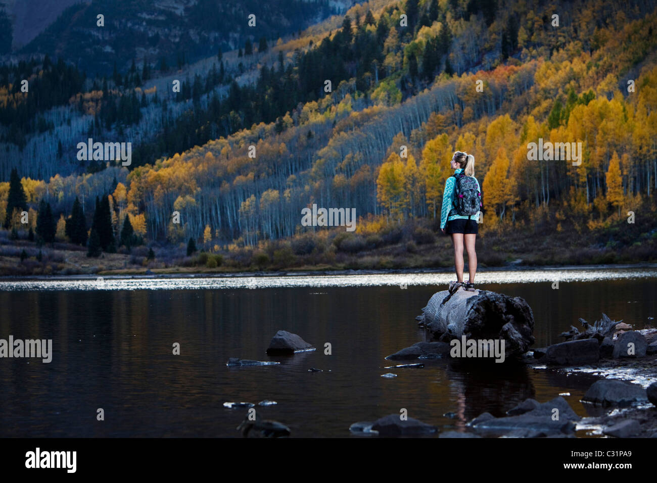 Una giovane donna escursionismo sorge su di un registro e prende in considerazione di i colori dell'autunno. Foto Stock