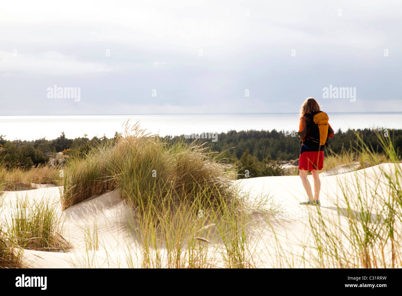 Una ragazza cammina da solo sulle dune di sabbia che indossa uno zaino. Foto Stock