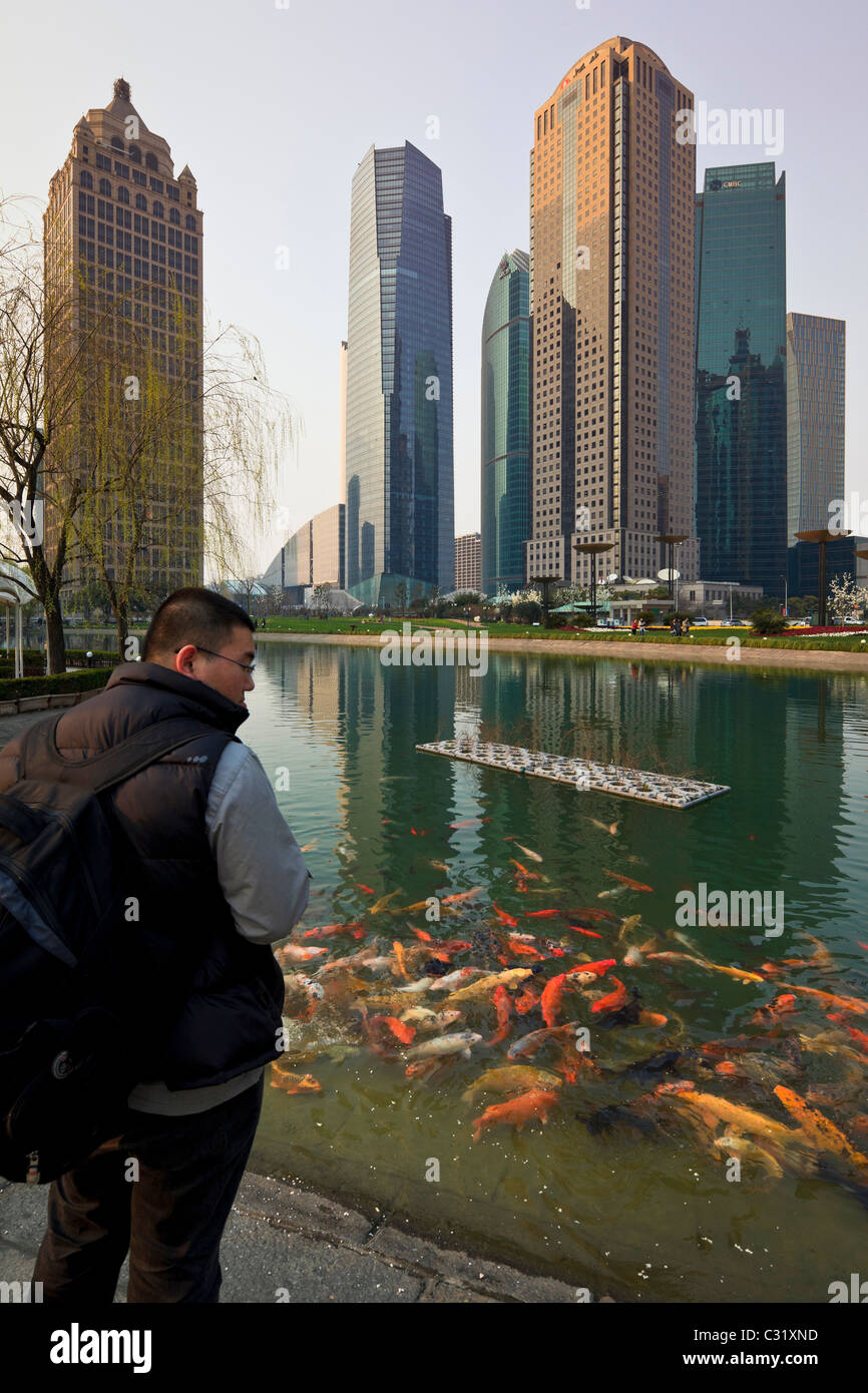 Un uomo alimentare pesce in uno stagno di pesci nella centrale di Lujiazui spazio verde del quartiere Pudong di Shanghai. Foto Stock