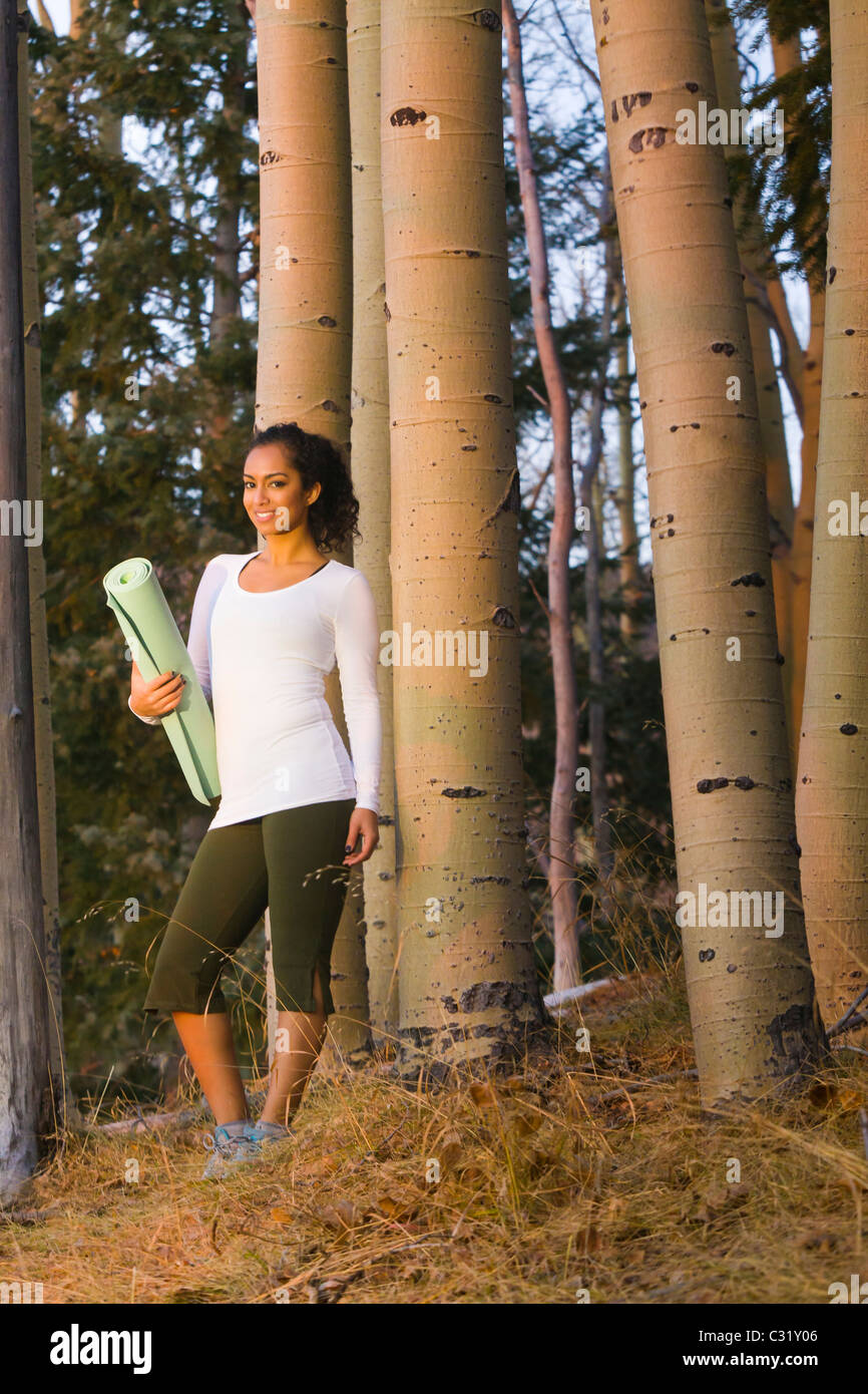 Razza mista donna azienda materassino yoga nella foresta Foto Stock