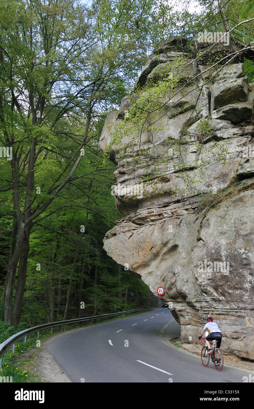 Ciclista in sella sotto la roccia arenaria formazione Predigtstuhl in Berdorf, piccola Svizzera / Mullerthal, Lussemburgo Foto Stock