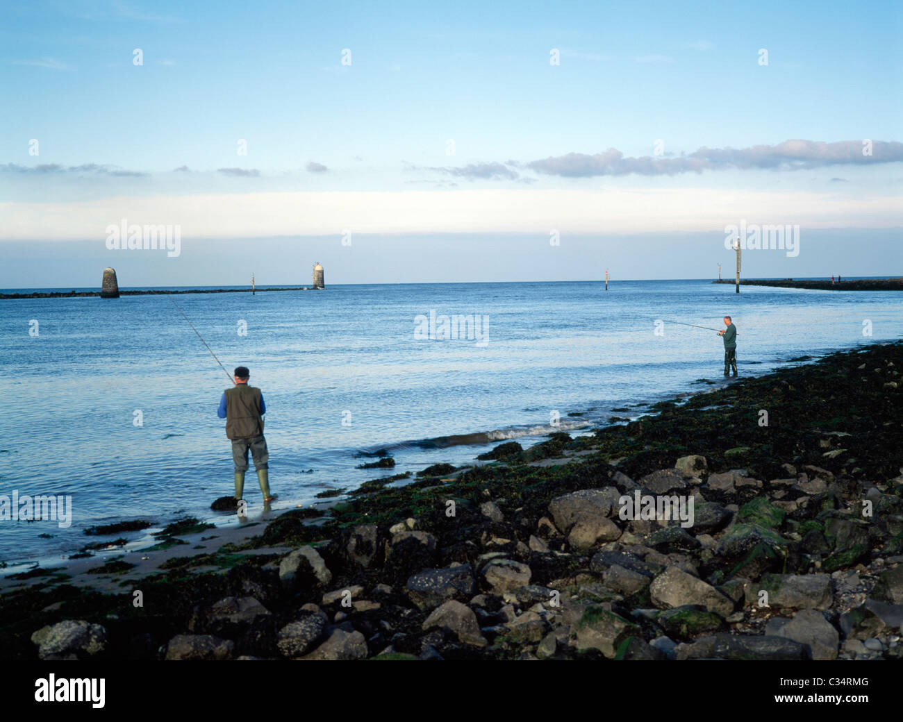 Gli uomini la pesca al largo spiaggia rocciosa Foto Stock