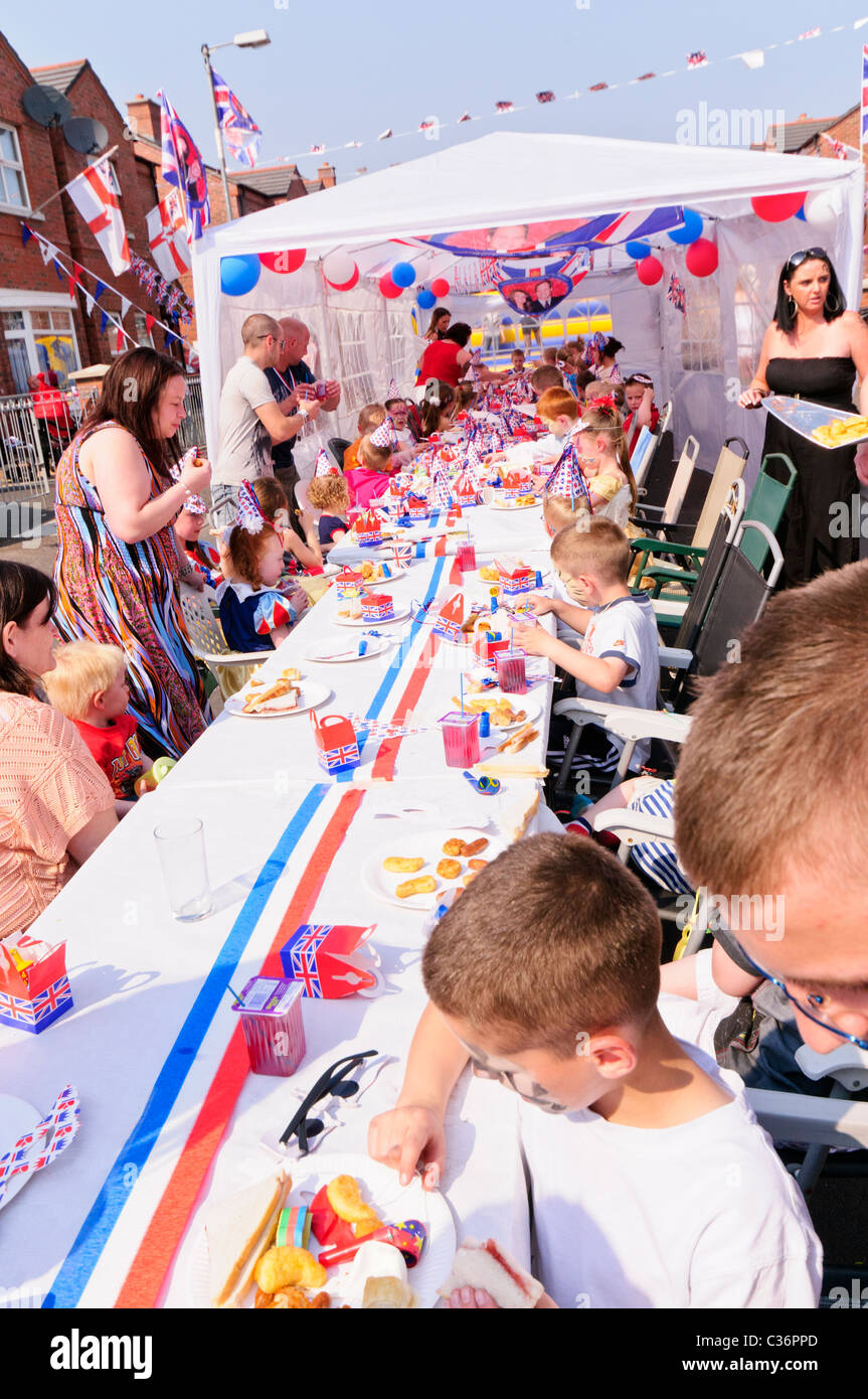 I bambini si siedono a lunghi tavoli con rosso, bianco e blu gli accessori di altri produttori a un evento reale partito di strada Foto Stock