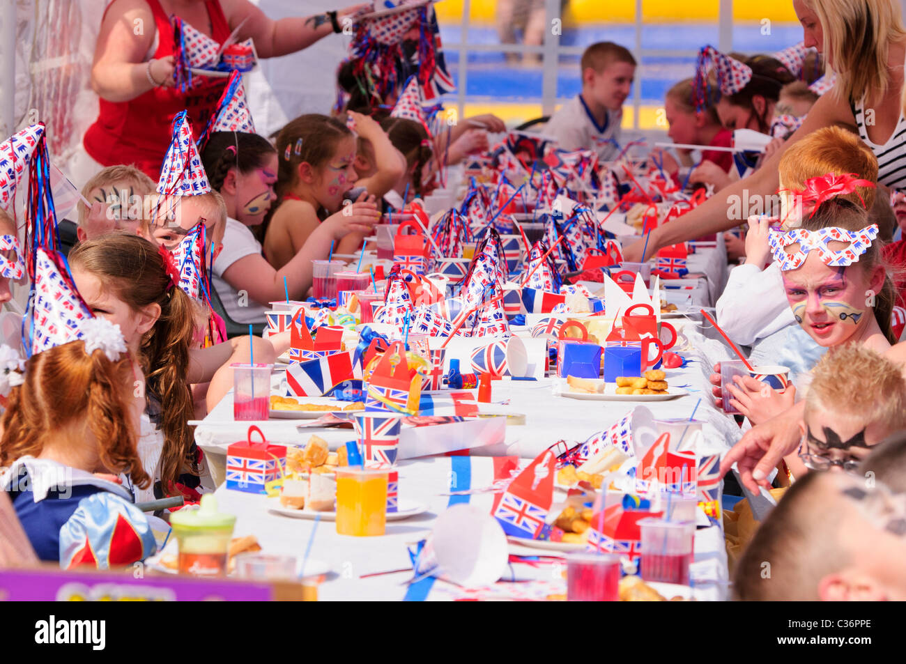 I bambini si siedono a lunghi tavoli con rosso, bianco e blu gli accessori di altri produttori a un evento reale partito di strada Foto Stock