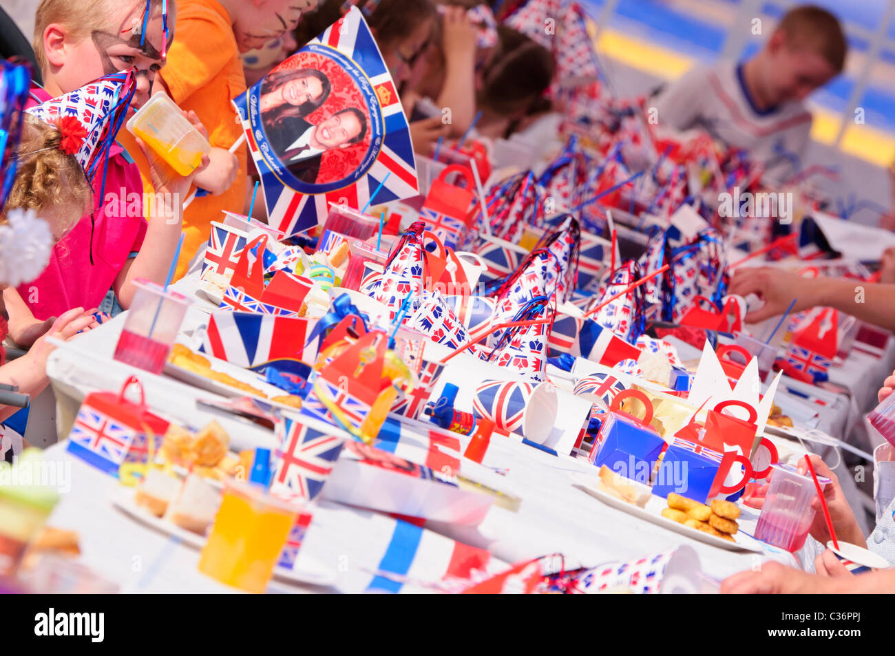 I bambini si siedono a lunghi tavoli con rosso, bianco e blu gli accessori di altri produttori a un evento reale partito di strada Foto Stock