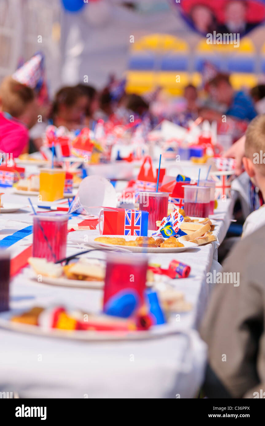 I bambini si siedono a lunghi tavoli con rosso, bianco e blu gli accessori di altri produttori a un evento reale partito di strada Foto Stock