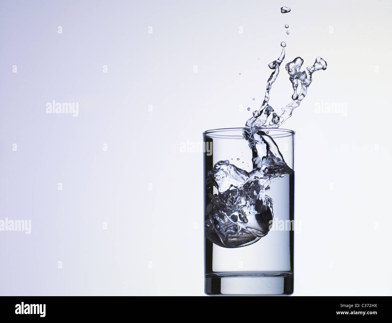 Cubo di ghiaccio che cade in un bicchiere di acqua Foto Stock