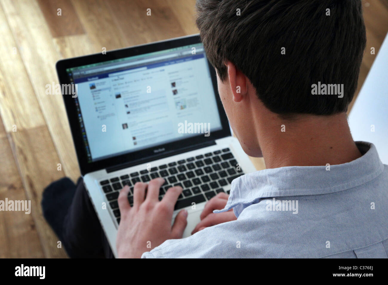 Oltre la spalla colpo di un giovane uomo che utilizza il suo computer portatile su una pagina di Facebook. Foto Stock