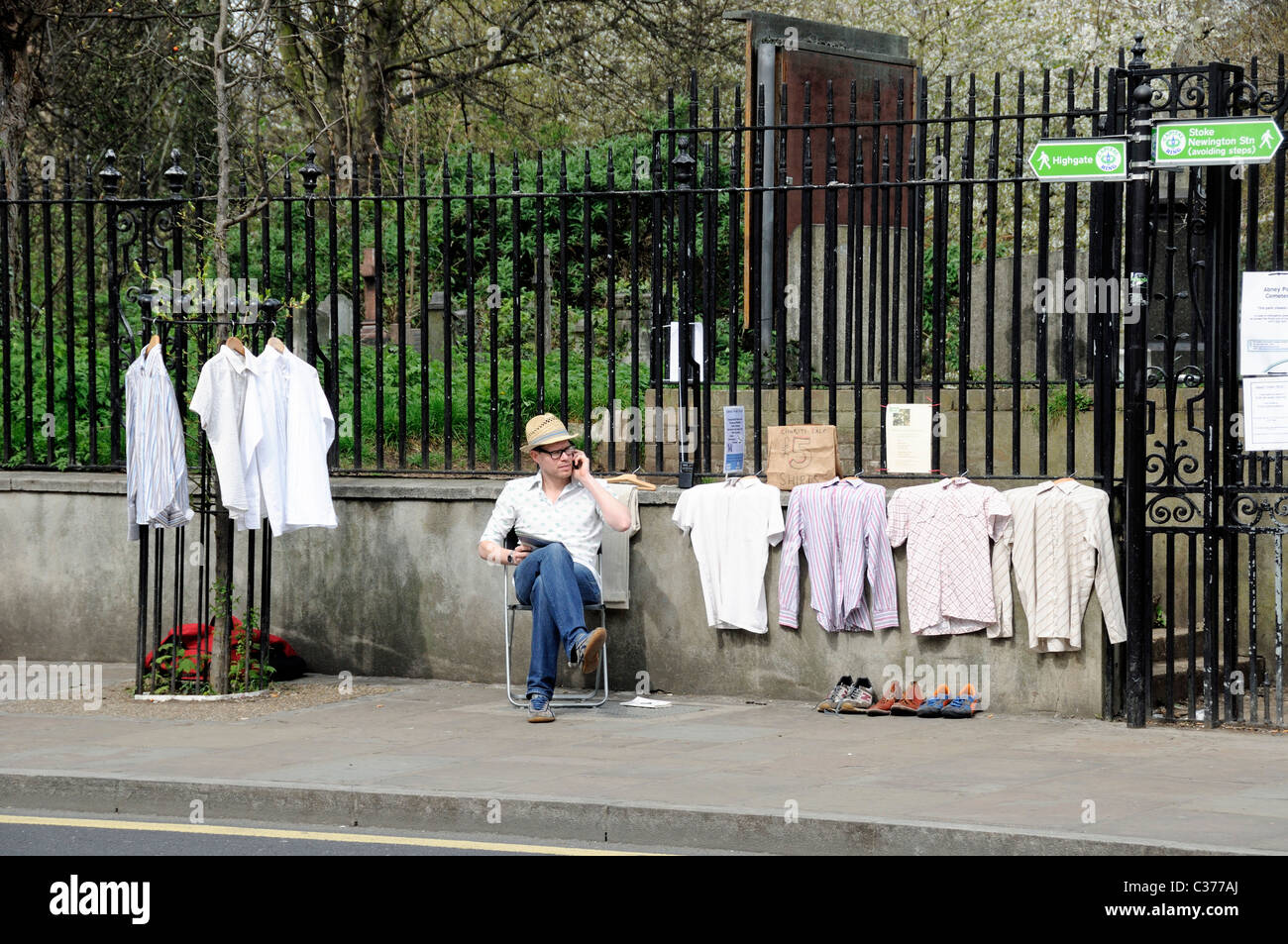Uomo seduto su una sedia con camicie in vendita in street, Stoke Newington Church Street Hackney Londra Inghilterra REGNO UNITO Foto Stock