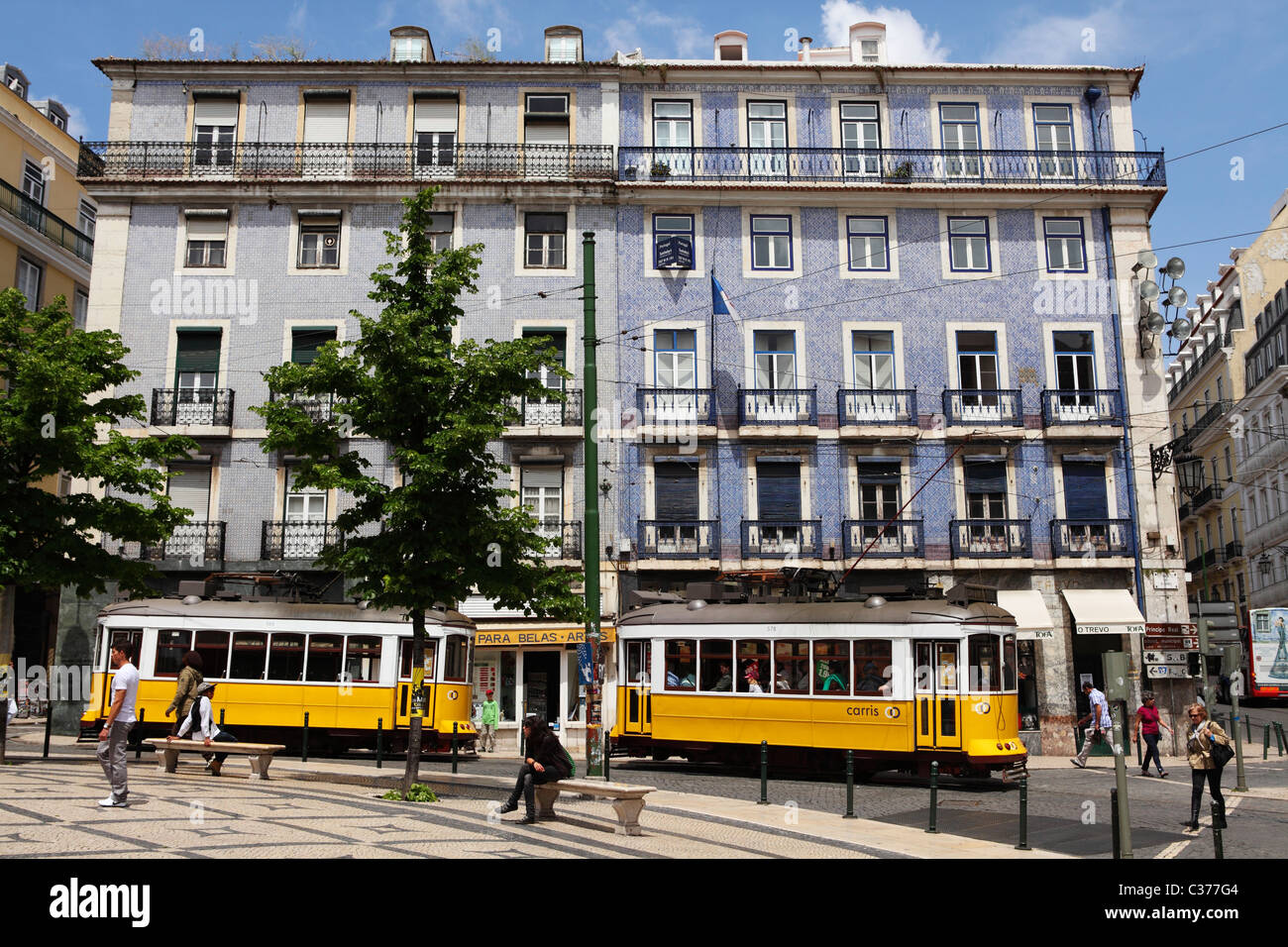 I tram passano passato una piastrella Azulejo edificio coperto sul largo Camoes di Lisbona, in Portogallo. Foto Stock