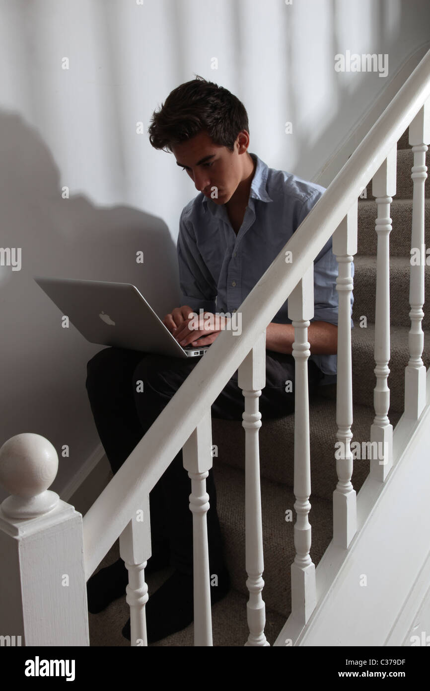 Giovane maschio seduto da solo sulle scale sorridente guardando al suo computer portatile Foto Stock