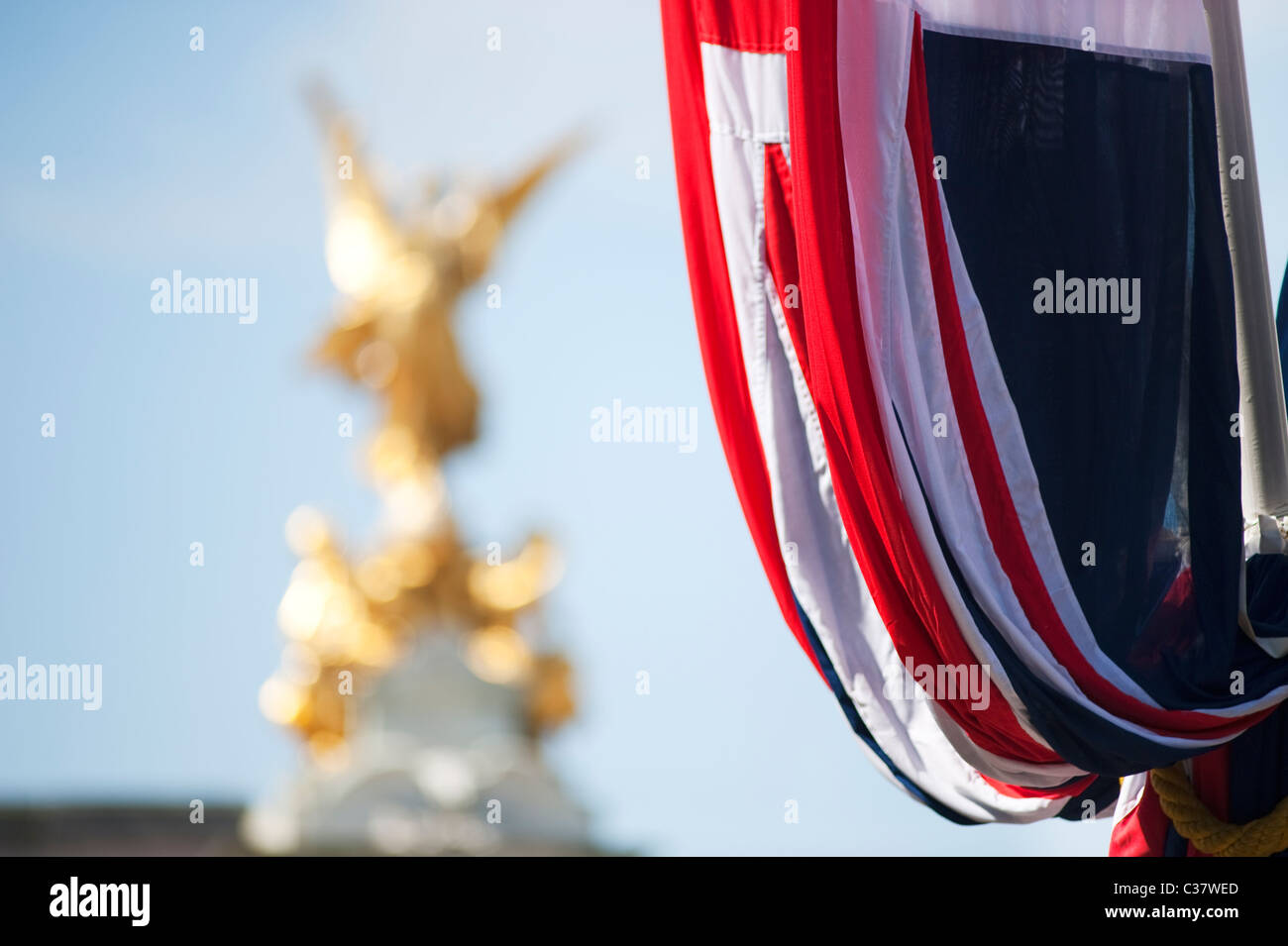 Bandiera dell'Unione appendere fuori Buckingham Palace con la statua dorata sulla sommità del memoriale della Victoria. Foto Stock
