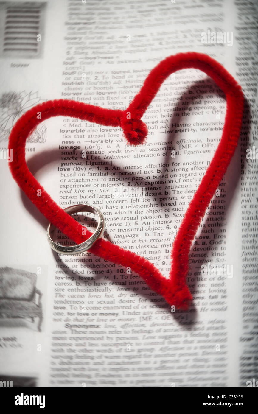 Un cuore rosso con un argento wedding band avvolta ad anello su di esso con il cuore che circonda la definizione di amore da parte del dizionario Foto Stock