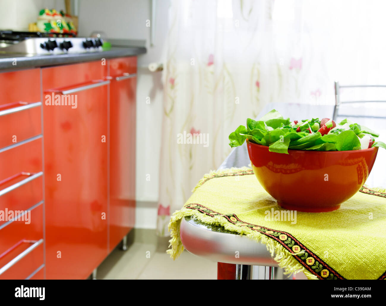 Recipiente rosso con insalata sul tavolo in cucina Foto Stock