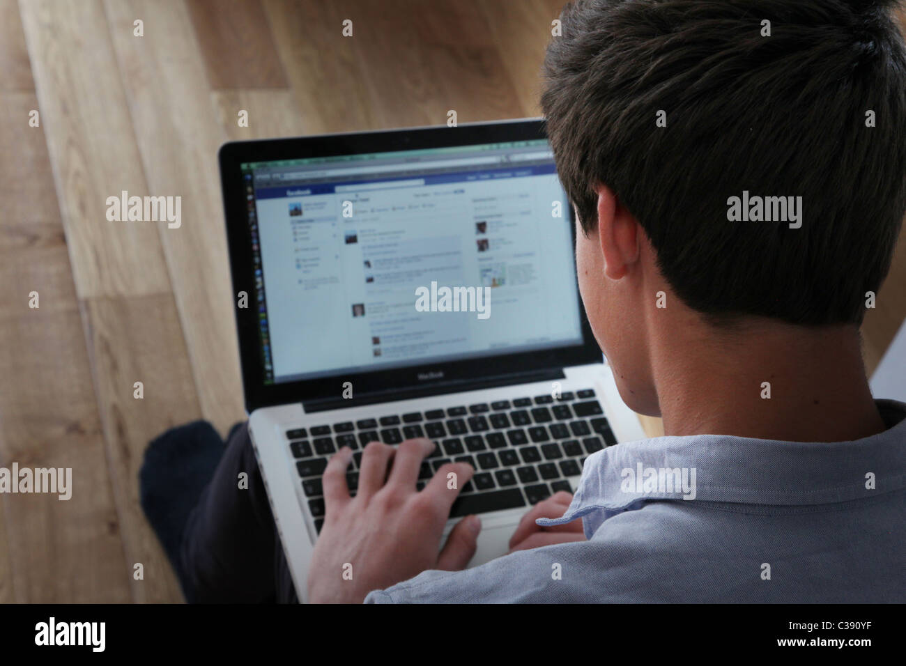 Maschio adolescente usando il suo computer portatile su una pagina di Facebook, shot sulla sua spalla. Foto Stock