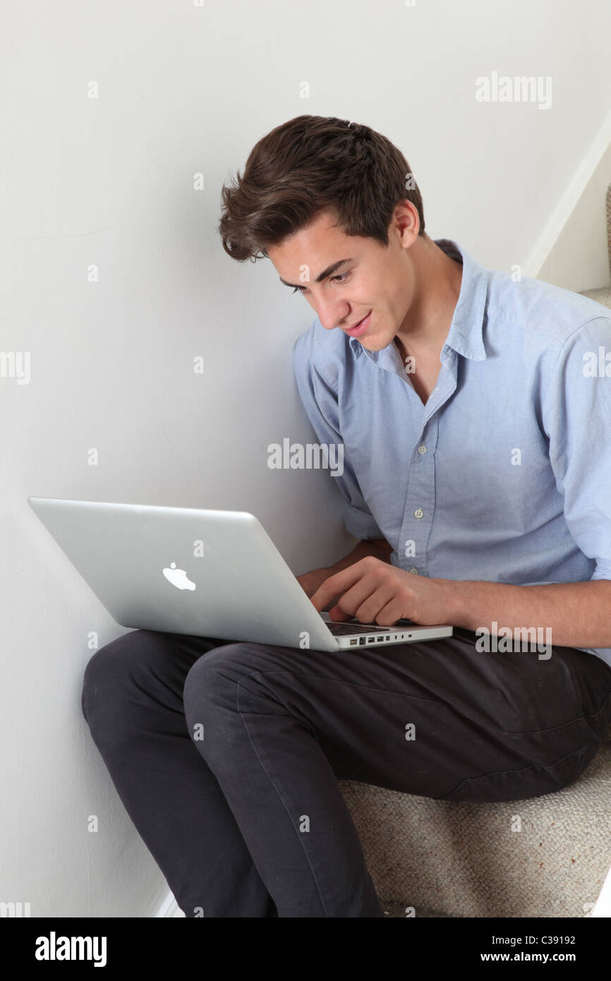 Giovane maschio seduto da solo sulle scale sorridente guardando al suo computer portatile Foto Stock
