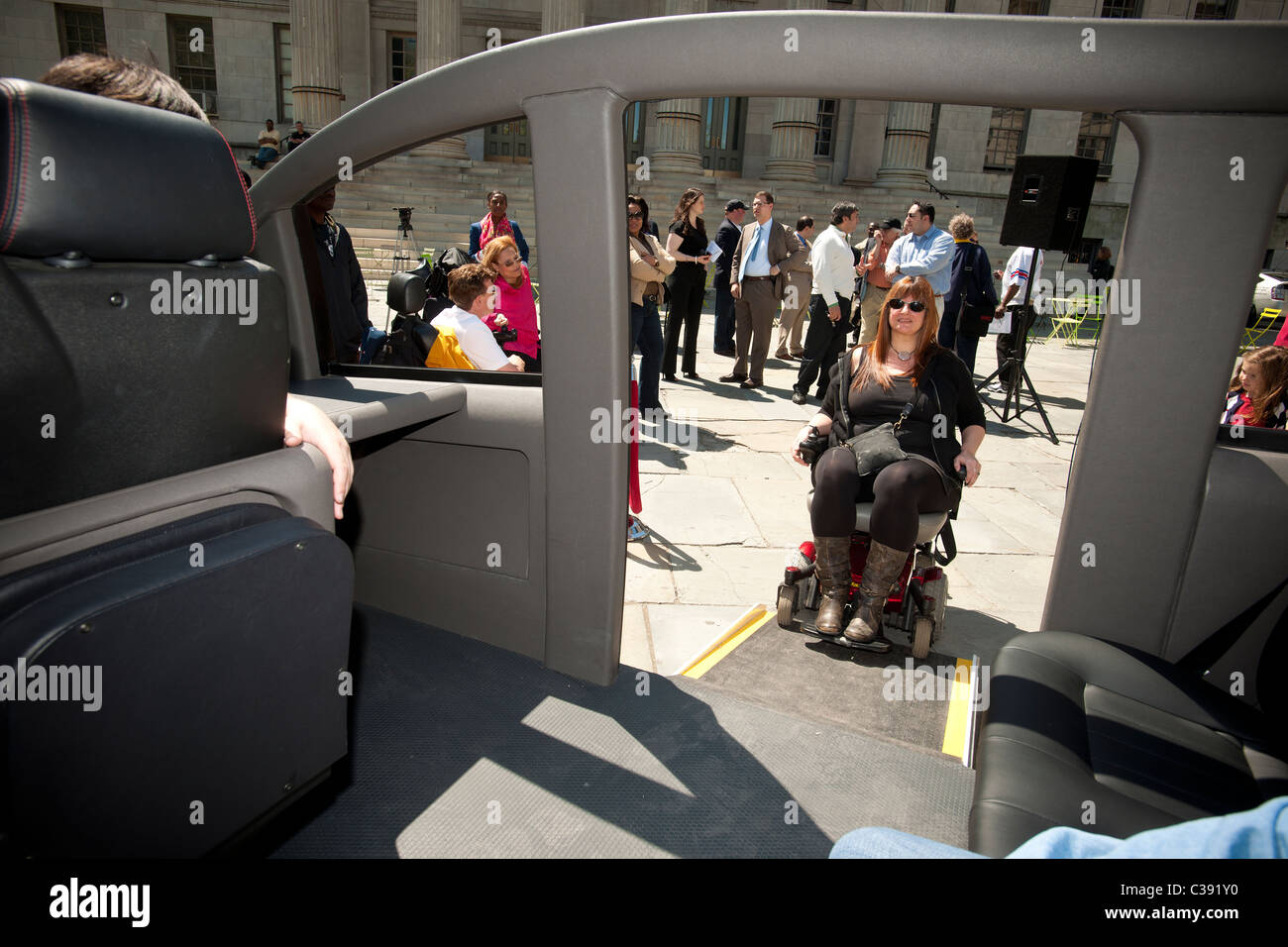 Una donna su una sedia a rotelle dimostra la rampa per disabili di un mock up del Karsan V1 taxi in New York Foto Stock